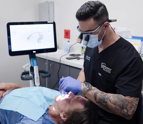 Dentist examining patient in clinical setting with digital display monitor visible overhead.
