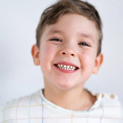 Young boy smiling broadly at camera against white background, dental health portrait.