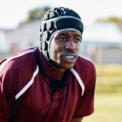 Athletic man wearing maroon sports jacket and protective headgear outdoors on field.