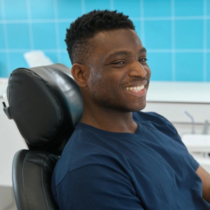 Smiling patient reclines in dental chair at modern dental office with blue tile background.