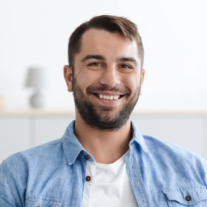 Smiling male dental professional wearing blue shirt in bright clinical office setting.