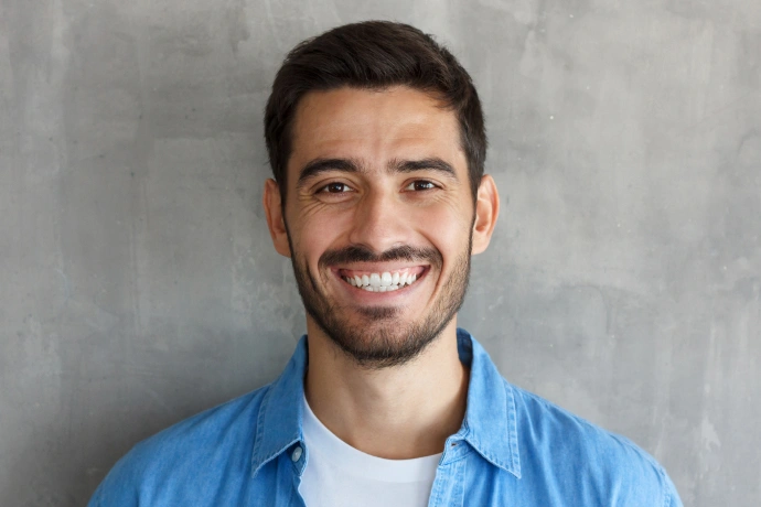 Smiling male dental professional in blue shirt against gray background, headshot portrait.