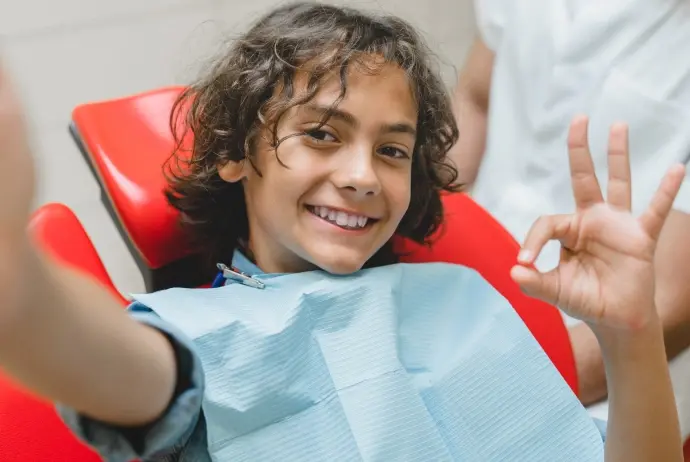 Happy child in red dental chair giving thumbs up during Mesa dental visit.