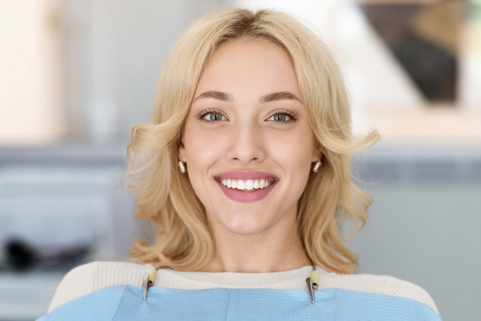 Smiling blonde woman in light blue top, professional headshot in dental office setting.