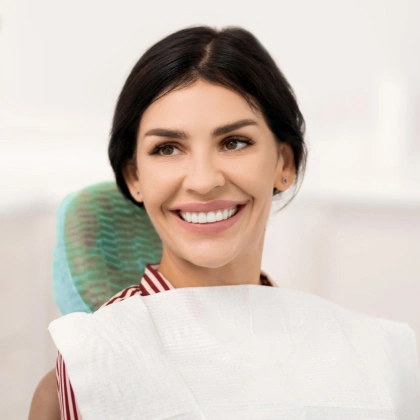 Smiling woman in dental office chair wearing white bib, green headrest visible behind.