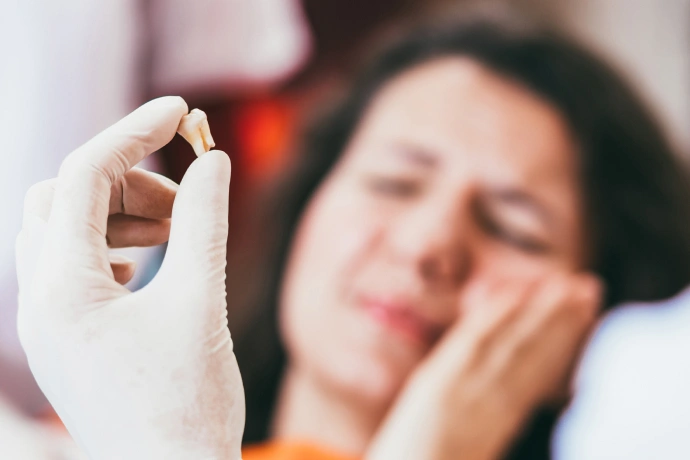 Woman holding medication pill with hand to face, appearing unwell or experiencing dental pain.