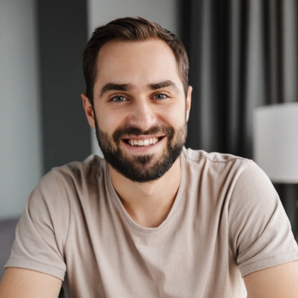Smiling man in beige t-shirt, professional headshot in modern interior setting
