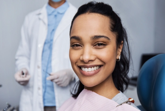 Young woman smiling in dental chair with dentist in background at clinic.