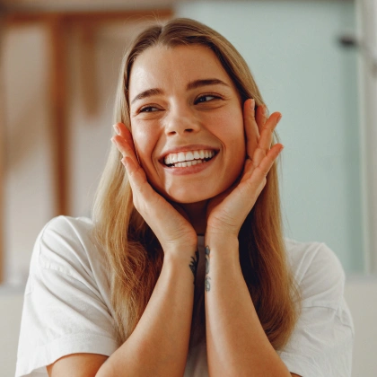Happy woman smiling with hands to face in bright dental office setting.