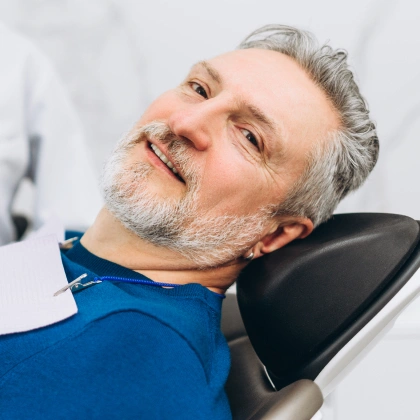 Mature man smiling in dental chair wearing blue bib at dental office.