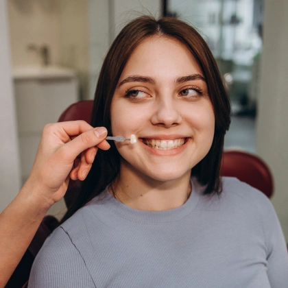 Young woman smiling while holding dental floss in modern dental office setting.