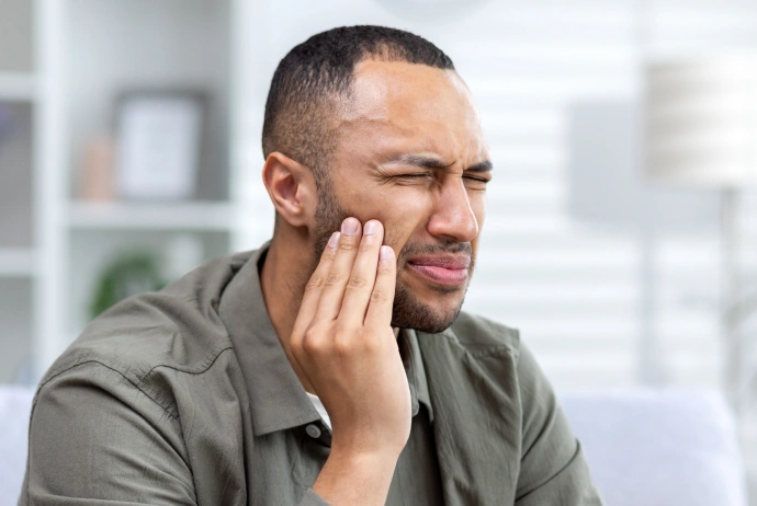 Man touching his cheek in pain or discomfort, sitting indoors with blurred office background.