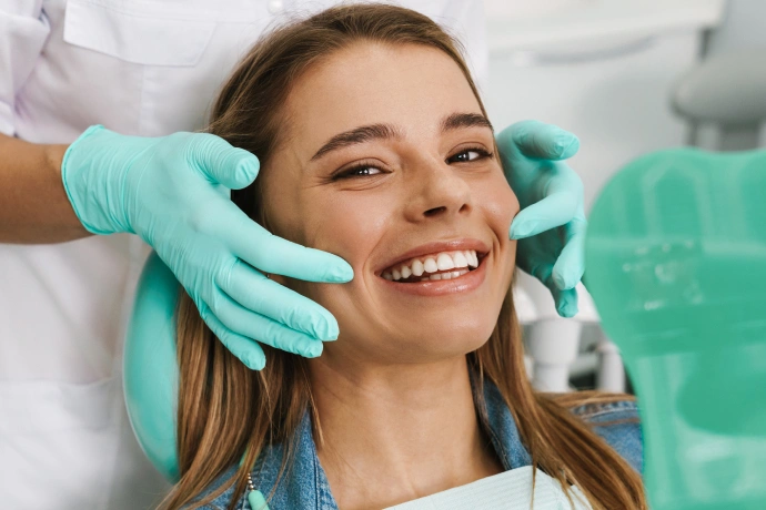 Smiling woman receiving dental examination from dentist wearing turquoise gloves in clinical setting.