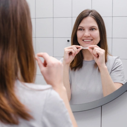 Woman brushing teeth at bathroom mirror with white tile background.