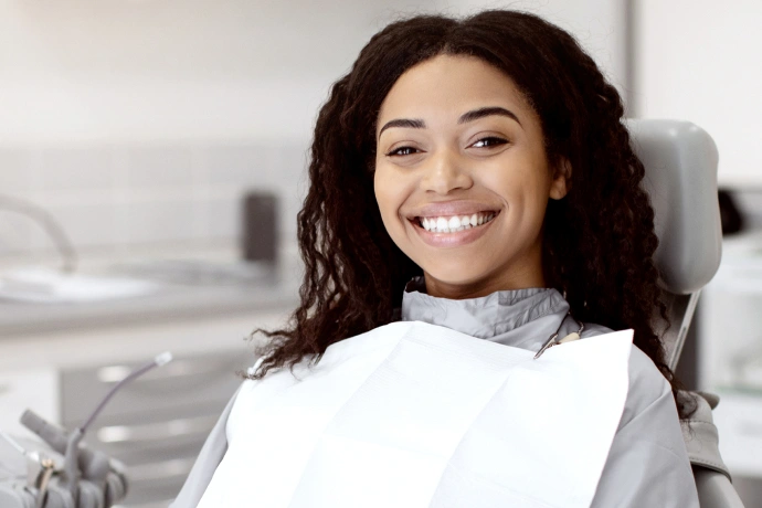 Smiling woman in dental bib seated in modern dental office chair