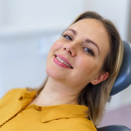 Woman in yellow shirt smiling at dental office, reclined in dentist chair.