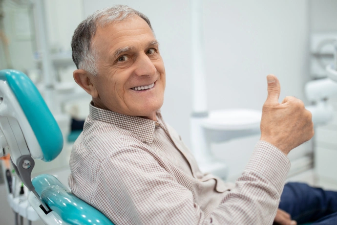 Smiling male patient giving thumbs up in modern dental office chair