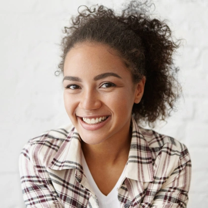 Young woman smiling at camera wearing plaid shirt against white background.