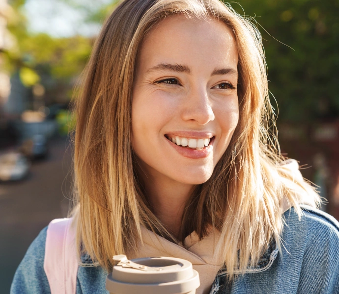 Young woman smiling outdoors in casual blue shirt with blurred green background.