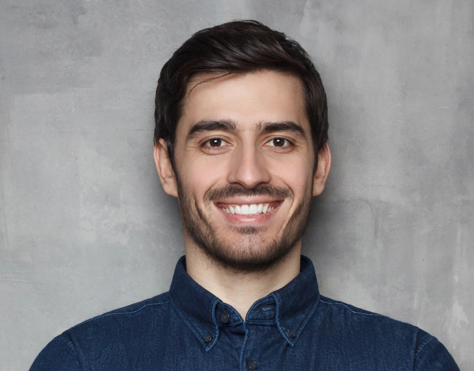 Male dental professional smiling at camera wearing navy blue shirt against gray background
