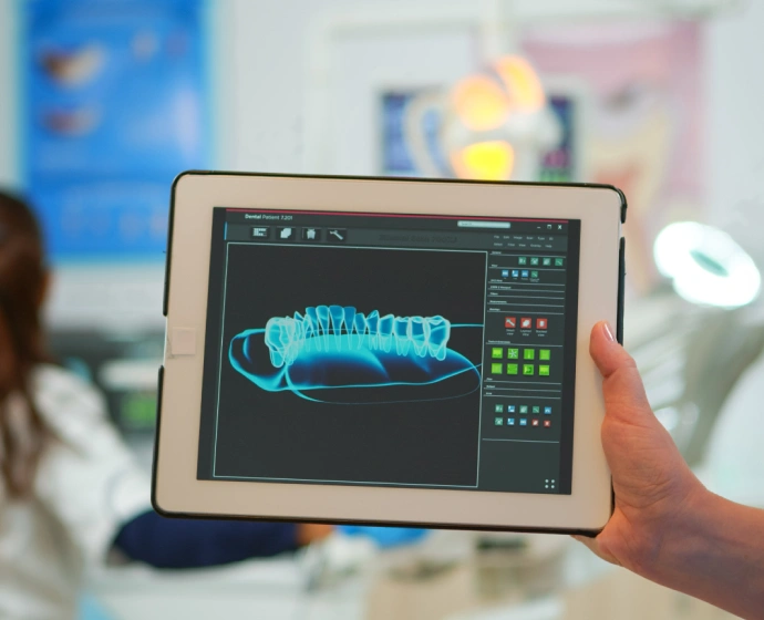 Person holding tablet displaying 3D dental scan model in modern dental office setting.