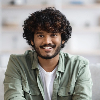 Smiling man with curly dark hair wearing sage green shirt in dental office setting.