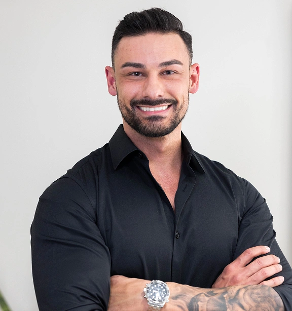 Professional male dental staff member smiling with arms crossed against white background.