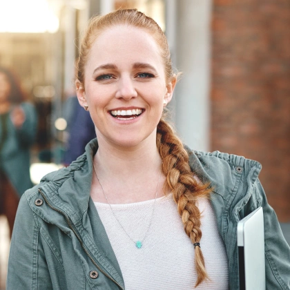 Young woman with braided hair smiling outdoors in casual denim jacket.