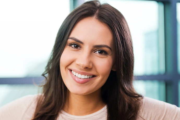 Professional headshot of a smiling woman in modern office setting with large windows.