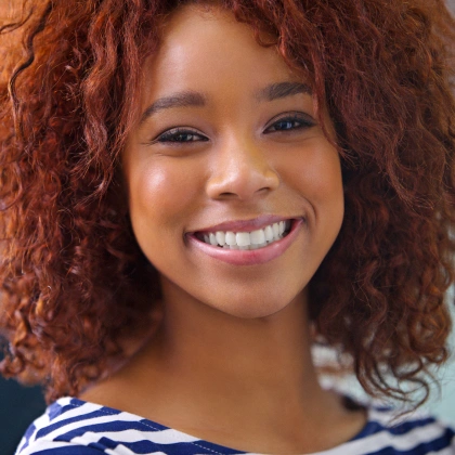 Smiling woman with curly reddish-brown hair in casual striped shirt, professional headshot.