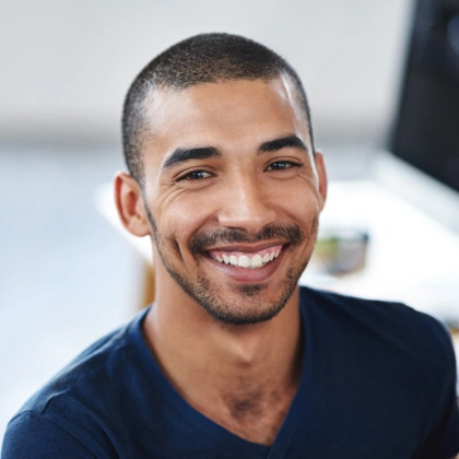Smiling man in dark blue shirt, professional headshot in dental office setting.