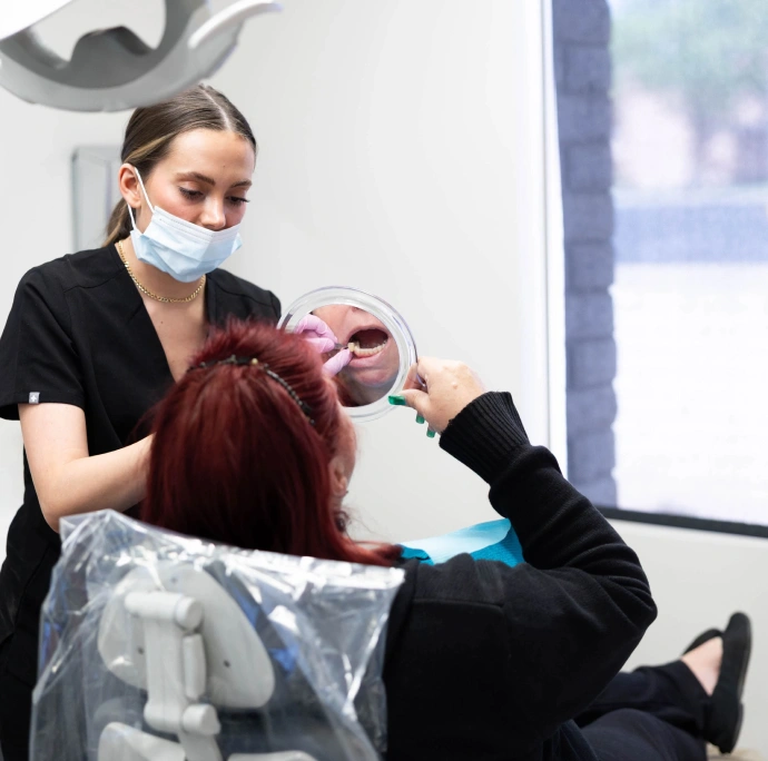 Dental hygienist wearing mask examines patient's teeth in modern dental office setting.