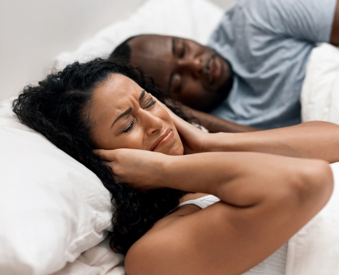 Woman resting in bed with hand to face, appearing to experience tooth or jaw pain.