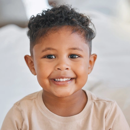 Smiling young child wearing beige shirt against blurred indoor background.