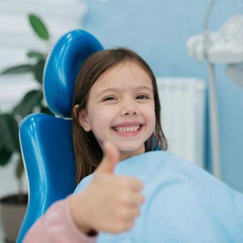 Young girl smiling in blue dental chair giving thumbs up at modern dental office.