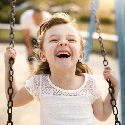 Happy child laughing on swing at playground during sunny day