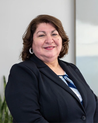 Professional woman in dark blazer smiling at camera in modern office setting.