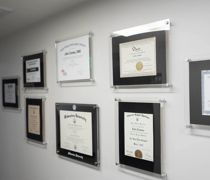 Framed dental certificates and licenses displayed on white wall in professional office setting.