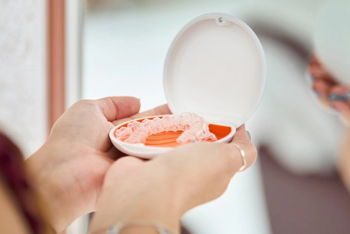 Child's hands holding open dental retainer case with clear orthodontic device inside