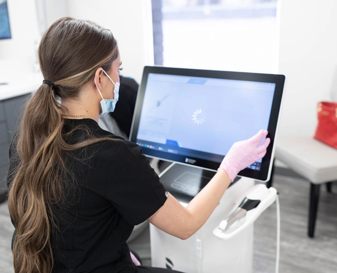 Woman with long brown hair wearing black shirt using touchscreen dental display monitor in clinical setting.