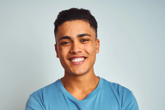 Young man smiling at camera wearing blue shirt against light blue background