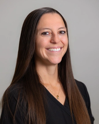 Professional headshot of woman smiling at Brown Road Dental against neutral gray background.