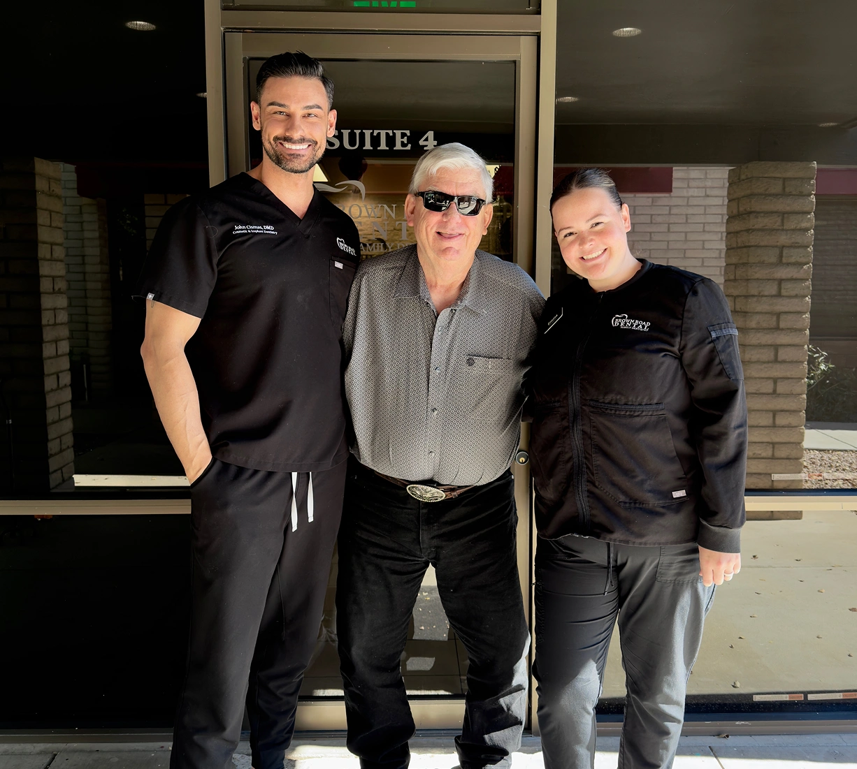 Three people posing together outside Brown Road Dental office at night.