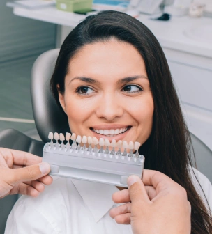 Woman holding dental shade guide in dental office setting, smiling at camera.