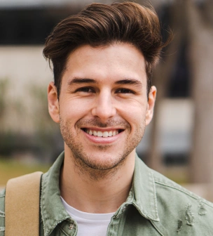Young man smiling at camera wearing green jacket outdoors in dental practice setting.