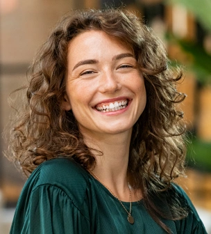 Smiling woman with curly brown hair wearing dark green shirt in dental office setting.