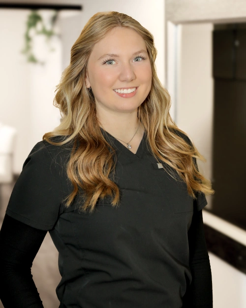 Professional woman smiling at camera in modern dental office setting wearing black top.