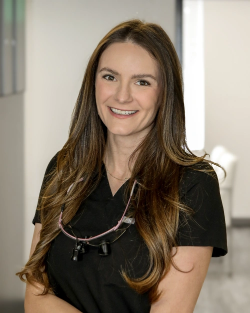 Professional headshot of smiling woman in black scrubs at dental office