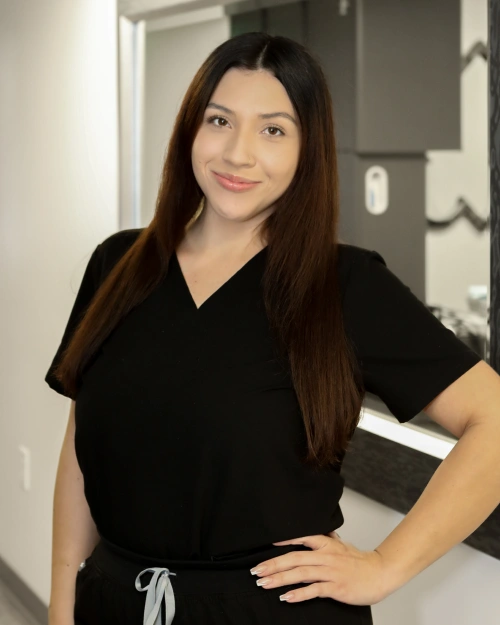 Woman in black scrubs smiling at camera in dental office setting.