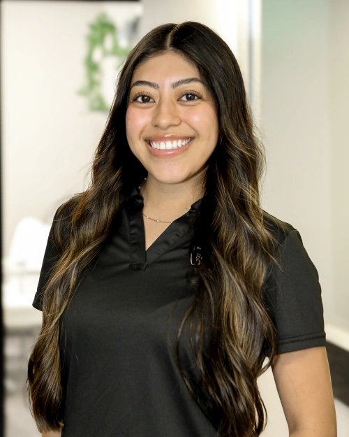 Young woman smiling at camera wearing black polo shirt in dental office setting.